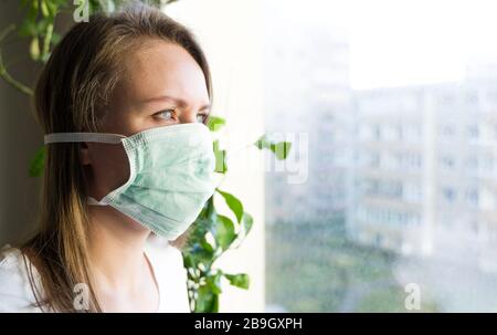 Frau in medizinischer Maske in der Nähe des Fensters. Quarantäne zu Hause. Stockfoto