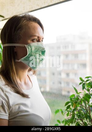 Frau in medizinischer Maske in der Nähe des Fensters. Quarantäne zu Hause. Stockfoto