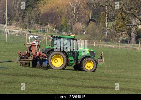 Ein Bauer treibt einen Traktor an, der Gülle über ein Feld verteilt. Stockfoto