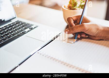 Nahaufnahme der Hand der berufstätigen Frau mit dem Laptop und Schreiben von Brief auf Notizbuchpapier im Büroschreibtisch. Der Lebensstil von Unternehmen und Menschen. Finanziell an Stockfoto