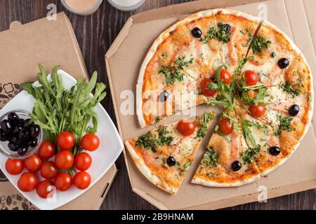 Pizza mit dünner Kruste und Lachs in Kartonverpackung Stockfoto