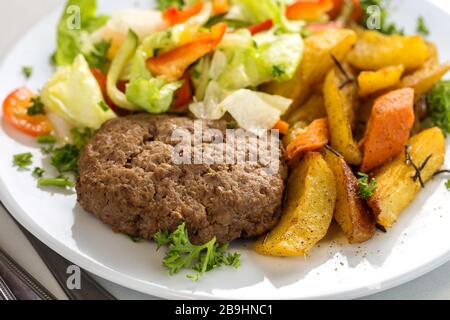 Leckeres Rindfleisch Burger Patty mit Salatgarnierung und Kartoffelspalten Stockfoto