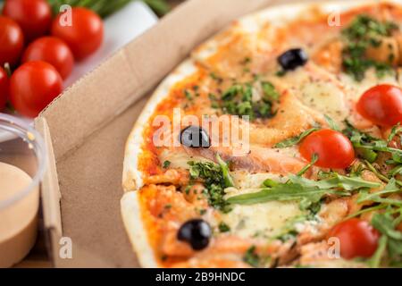 Köstliche italienische Pizza mit Lachs, Tomaten, Arugula und Käse in Pappkarton Stockfoto