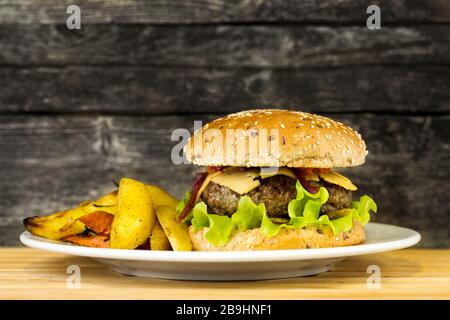 Leckerer gegrillter Rinderburger mit Kartoffelkeilen auf einem Teller auf rustikalem Holzhintergrund Stockfoto