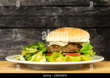 Delikat gegrillter Rinderburger auf rustikalem Hintergrund mit Salat auf einem Teller mit Kopienraum Stockfoto