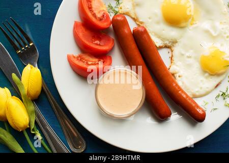 Spiegeleier mit Würstchen für die Frühstückswohnung lagen auf blauem Holzhintergrund Stockfoto