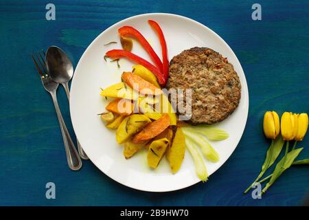 Saftige Rinderschnitzel mit Kartoffeln und Pfeffer auf blauem Holzgrund Stockfoto