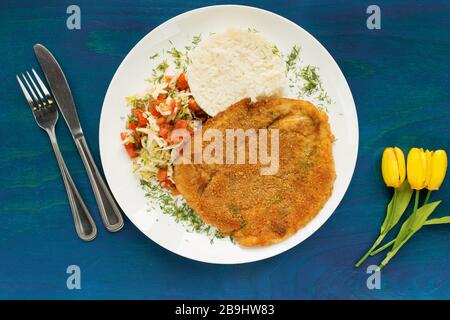 Hühnerfilet Schnitzel mit Reis und Salat auf blauem Holzhintergrund Stockfoto