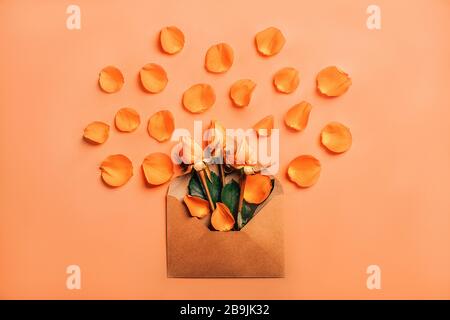 Handarbeit Briefumschlag mit orangefarbenen Rosen in Kronblättern auf Korallenhintergrund. Stockfoto