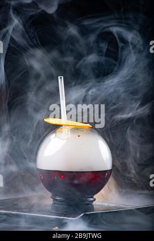 Kugelglas mit Rauch und Alkohol. Karamellisierte Zitronenscheiben. Rauch auf schwarzem Hintergrund. Stockfoto