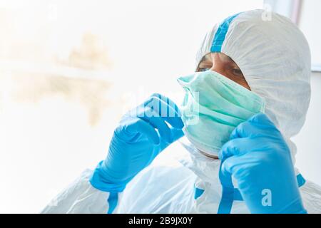 Arzt in der Klinik in Schutzkleidung zieht während der Covid-19-Epidemie auf eine Gesichtsmaske Stockfoto