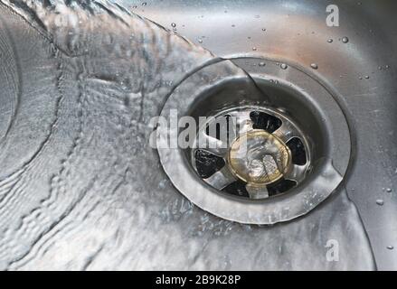 Eine Euro-Münze steckte in einem Spülbecken, in dem das Wasser darüber fließt Stockfoto