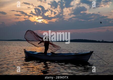 Ein Fischer wirft ein Netz bei Sonnenuntergang in einem berühmten See in uluabat bei Golyazi, Bursa, Türkei Stockfoto