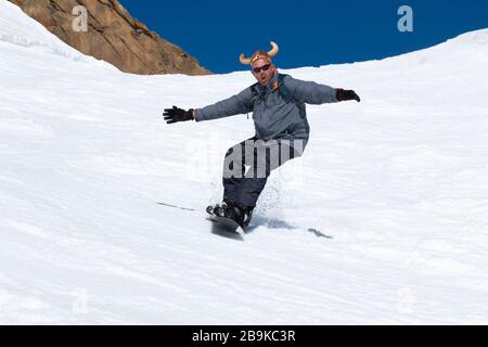 Snowboarder, der im Skigebiet mit einem lustigen Hut die Piste hinunterläuft. Wintersport und Erholung, Freizeitangebote im Freien. Sportkonzept Stockfoto