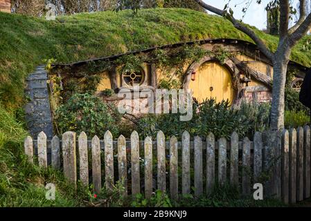 Abendlicht beleuchtet die runde, gelbe Tür eines Hobbitlochs am Hobbiton Movie Set, Neuseeland