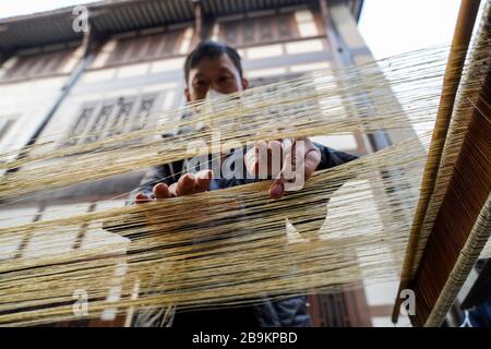 (200324) -- CHONGQING, 24. März 2020 (Xinhua) -- EIN Techniker macht Rongchang Grass Linen, auch Rongchang Xiabu genannt, in einem Workshop im Rongchang District in Chongqing, Südwestchina, 23. März 2020. Rongchang Grass Leinen ist ein traditionelles chinesisches Handwerk mit einer reichen Geschichte. Es ist eine Art Tuch, das rein von Hand aus Ramie besteht und berühmt ist für seine weiche, dünne, flache Textur und feine Qualität. Da dieses Tuch den Körper normalerweise im heißen Sommer kühl hält, wird es auch Xiabu (wörtlich Sommertuch) genannt. Mit umfassenden epidemischen Präventionsmaßnahmen macht Xiabu hier Industrien Stockfoto