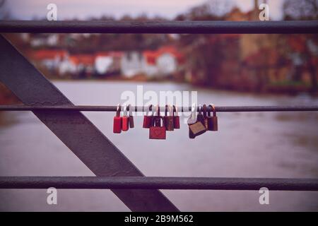 Lovelocks hängt an einem Brückengeländer mit einem Fluss im Hintergrund. Romantische Vorhängeschlösser auf einer Brücke in symmetrischer Reihe. Symbol der unzerbrechlichen Liebe. Stockfoto
