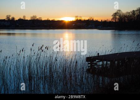 Schöner Sonnenuntergang auf dem Wasser auf einem blauen See oder Fluss mit einer Silhouette von Wald Stockfoto