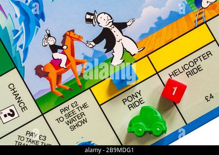 Junior Monopoly-Brettspiel - Detail des grünen Auto-Tokens auf Pony-Ride-Platz mit Haus und roten Würfeln, die 1 zeigen Stockfoto