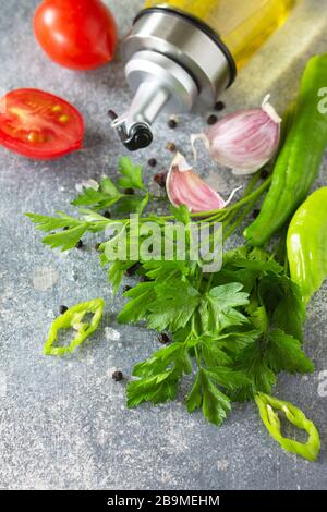 Gewürze, Kräuter und Grüns im Hintergrund. Auswahl an Gewürzen, Kräutern und Olivenöl auf einem Steintisch. Stockfoto