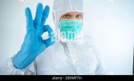 kaukasischer Arzt mit Schutzanzug und Maske, der eine Geste mit Ja unterschreibt, was zu einer positiven Signalwirkung führt. Schließen Sie die Viruserkrankung ab. Isoliert auf weißem Hintergrund. Stockfoto