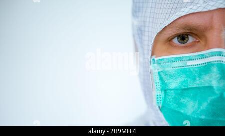 Ein Nahporträt eines selbstbewussten männlichen kaukasischen Arztes, der einen Schutzanzug und eine auf weißem Hintergrund isolierte Operationsmaske trägt. Medizinisch und alt Stockfoto