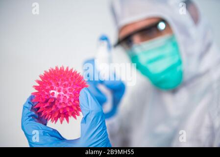 Arzt im Schutzanzug verwenden Sie Desinfektionsmittel für das rote Coronavirus Modell. Hand, die ein antibakterielles Gel hält. Vorbeugende Maßnahmen gegen Covid-19-Infektionen. Stockfoto