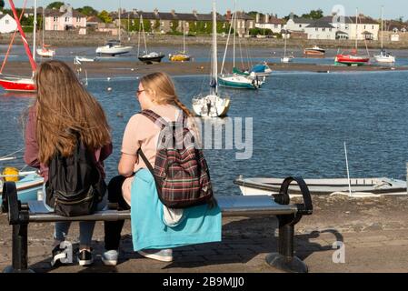 Rückansicht von zwei kaukasischen Teenagern, die auf einer Bank am Davitt's Quay Town Marina in Dungarvan, County Wexford, Irland sitzen Stockfoto