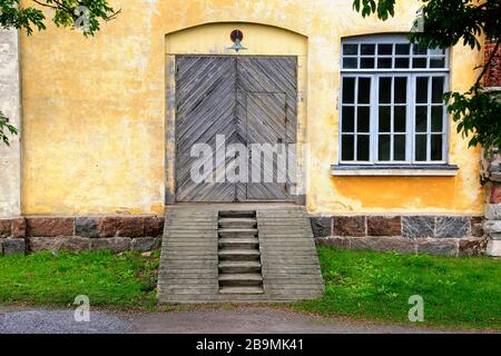 Fassade aus altem gelbem Steinbau in Suomenlinna, Finnland mit gewölbter Holztür mit Rampe und Bogenfenster. Stockfoto