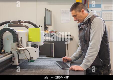 Der Techniker der Druckerei arbeitet an einer großen CNC-Computer- numerischen Steuerungs- und Schneidemaschine Stockfoto