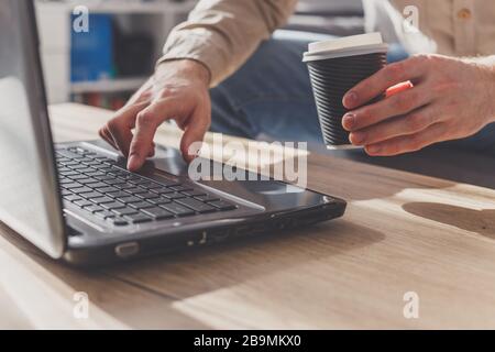 Freiberufler arbeiten von zu Hause aus mit einer Tasse Kaffee aus Papier auf dem Laptop Stockfoto