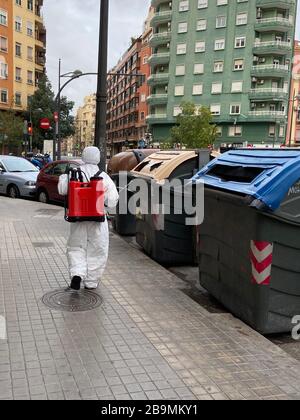 Spanische Regierung führt Straßendesinfektion gegen Coronavirus durch. Valencia Stadt. Mann in einem weißen Hazmat-Anzug mit rotem Spritzenrucksack. Stockfoto