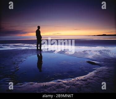Kanalinseln. Guernsey. Silhouette des jungen Mannes, der in der Dämmerung am Strand von Vazon steht. Stockfoto