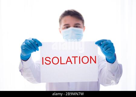 Ein Arzt in einem medizinischen Gown und einer Schutzmaske hält ein Zeichen, das Isolierung sagt. World Coronavirus Epidemie Kovid-19, Pandemie 2020 Stockfoto