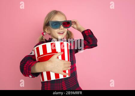 Gute 3D-Brille. Kaukasisches Kleinmädchenporträt auf pinkfarbenem Studiohintergrund. Schöne weibliche modelblonde Haare. Konzept menschlicher Emotionen, Gesichtsausdruck, Verkauf, Werbung, Kino, Kindheit. Stockfoto