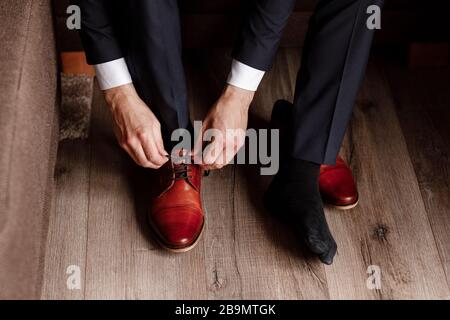 Der Bräutigam hat die Schnürsenkel an den Schuhen eng angeschnallt. Der Business man hängt Schuhe im Hotelzimmer in die Halle. Die Hände von Mans und Paar Lederschuhe für Herren. Besprechung von Stockfoto