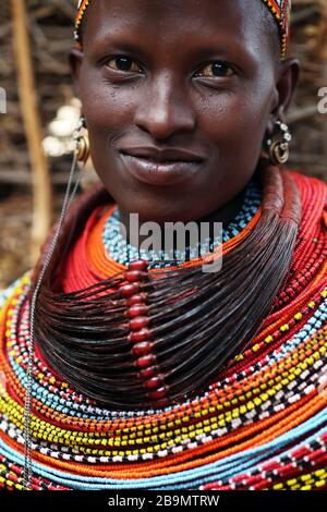 Eine junge Samburu-Frau, die in traditioneller Kleidung lächelt, in einem abgelegenen Samburu-Stammdorf in der Nähe von South Horr, Kenia. Stockfoto