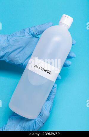 Hände mit Schutzhandschuh, der eine Flasche Alkohol hält. Desinfektionsmittel für Coronavirus Kovid-19-Ausbruch Stockfoto