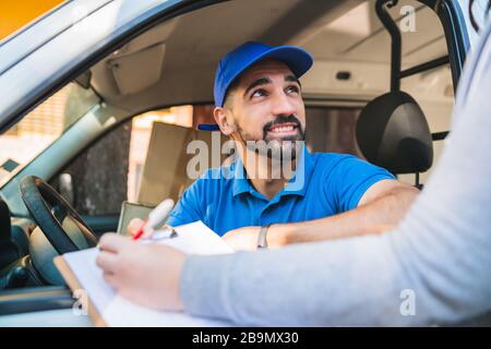 Portrait eines Lieferers im Lieferwagen, während der Kunde die Unterschrift in die Zwischenablage legt. Liefer- und Versandkonzept. Stockfoto