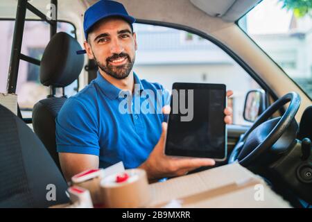 Portrait eines Zustellfahrers, der ein digitales Tablet verwendet, während er im Lieferwagen sitzt. Liefer- und Versandkonzept. Stockfoto