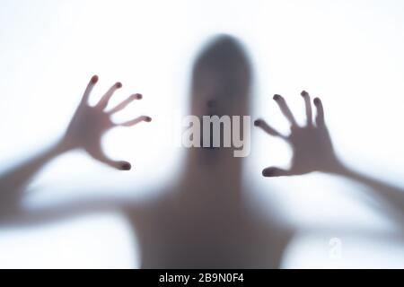 Verschwommener Silhouettenschatten einer terrorischen Körperform hinter einem weißen Hintergrund, der Kopf und knollige Finger zeigt. Horror-Konzept eines Besuchers von Out o Stockfoto