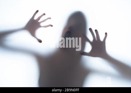 Verschwommener Silhouettenschatten einer terrorischen Körperform hinter einem weißen Hintergrund, der Kopf und knollige Finger zeigt. Horror-Konzept eines Besuchers von Out o Stockfoto