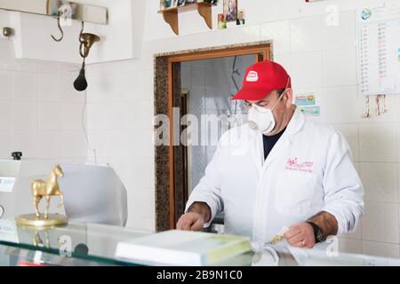 Avetrana, Italien, - Marth 19, 2020. Der Verkäufer serviert einem Kunden Fleisch, trägt medizinische Maske und Handschuhe Schutz während Coronavirus Epidemie. Schopp Stockfoto