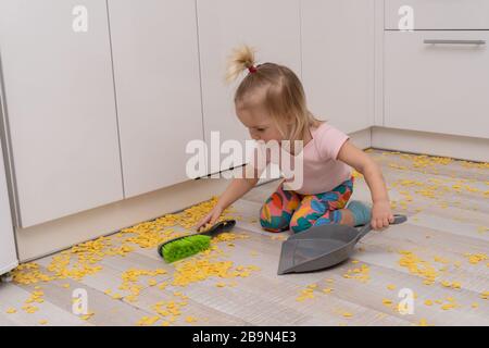 Süßes kleines kaukasisches Mädchen reinigt den Boden in der Küche. Stockfoto