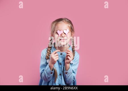 Kleines Mädchen, das ihre Augen hinter rosafarbenen Herzformen versteckt Stockfoto