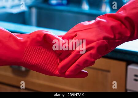 Zwei Personen halten bunt mit Latexgluten in einer Küche. Die Bilder illustrieren Menschen, die sich mit sozialer Distanzierung innerhalb des Hauses zwischen t beschäftigen Stockfoto