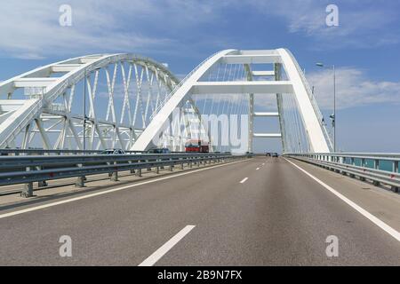 Krimbrücke über die Straße von Kertsch. Autos durchziehen die weiße Bogenspannweite. Sonniger Sommertag Stockfoto