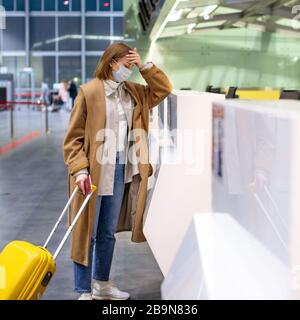 Frau mit Gepäck wegen Stornierung des Flugs verärgert, steht an leeren Check-in-Schaltern am Flughafenterminal wegen Coronavirus-Pandemie/Covid-19-Outb Stockfoto