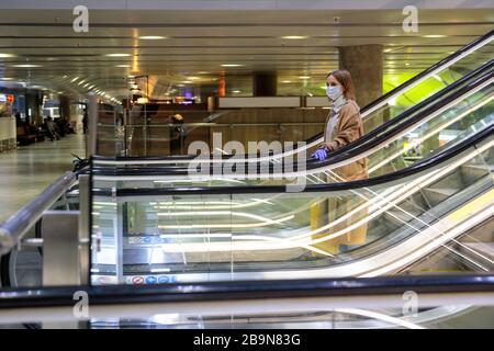 Frau mit gelbem Gepäck steht auf Rolltreppe, hält Rolltreppen-Handlauf im Flughafenterminal durch Latexhandschuhe, um sich vor Kontakt mit w zu schützen Stockfoto