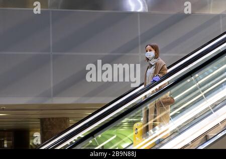 Frau mit gelbem Gepäck steht auf Rolltreppe, hält Rolltreppen-Handlauf im Flughafenterminal durch Latexhandschuhe, um sich vor Kontakt mit w zu schützen Stockfoto